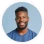 Portrait of a smiling man with short hair and beard wearing a blue shirt against a light background.